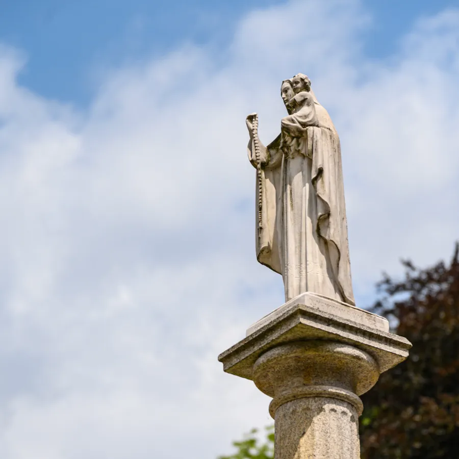 Statue of the Virgin Mary holding baby Jesus on a column, set against a cloudy blue sky