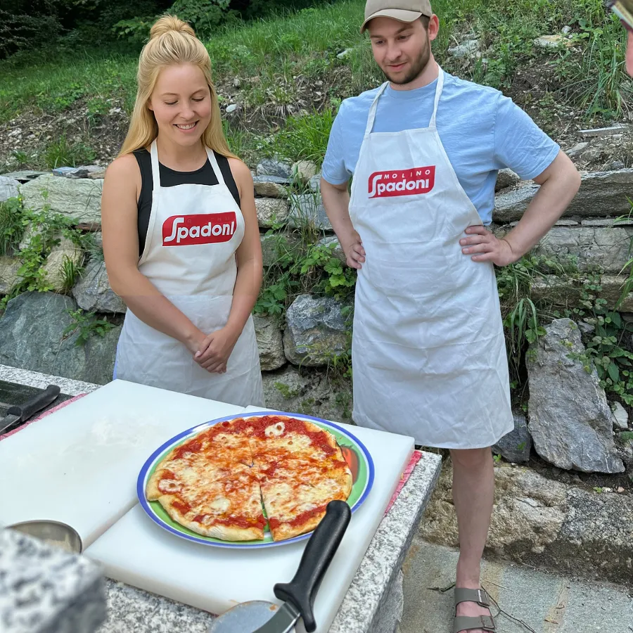 Couple wearing Molino Spadoni aprons proudly presenting a homemade pizza during an outdoor cooking class on Lake Como