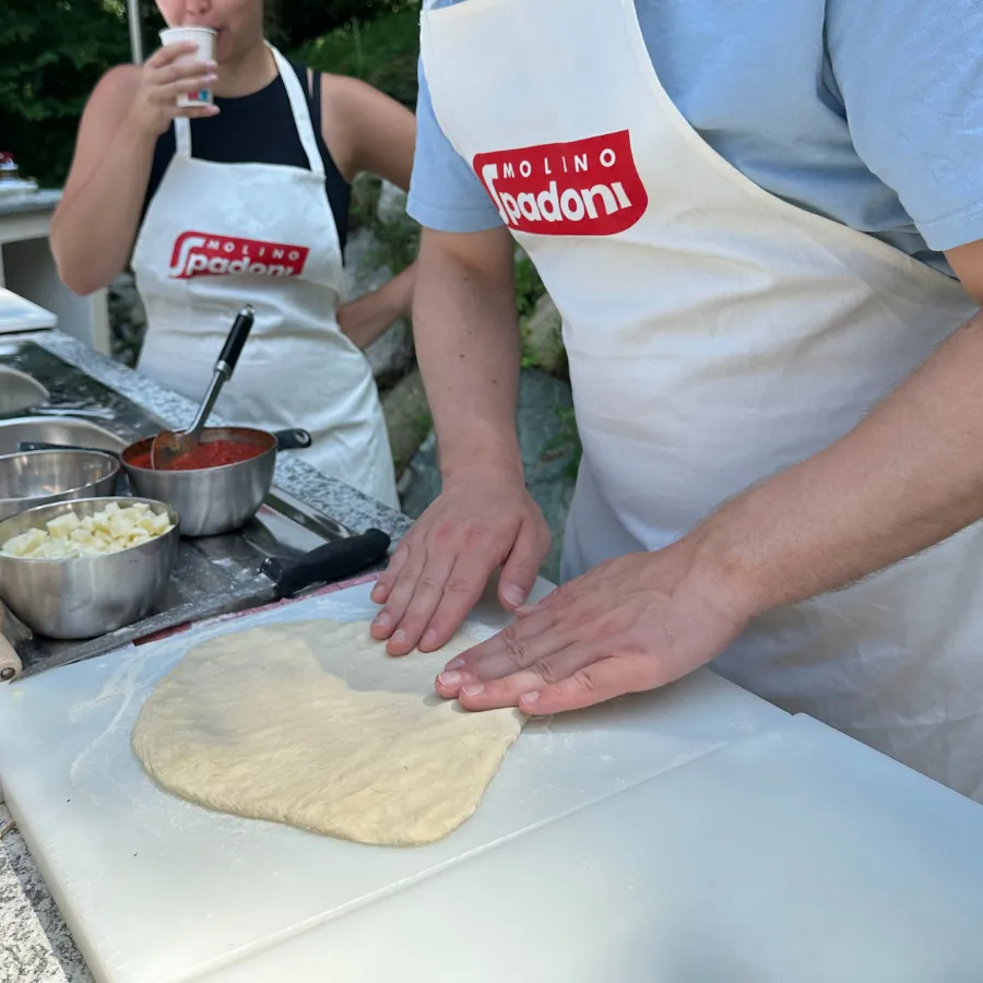 Pizza dough being hand-stretched by a participant at a traditional cooking class on Lake Como