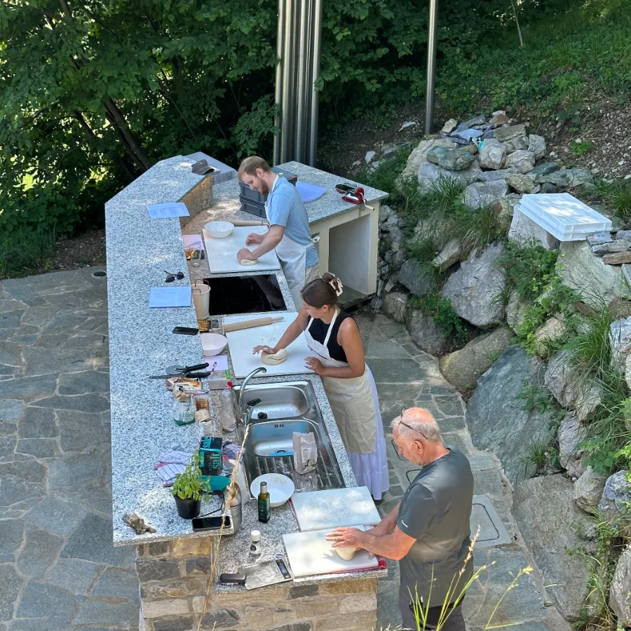 Aerial view of an outdoor cooking class with tourists kneading dough on stone countertops on Lake Como