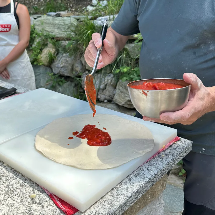 Chef spooning tomato sauce onto pizza dough during an authentic culinary experience on Lake Como