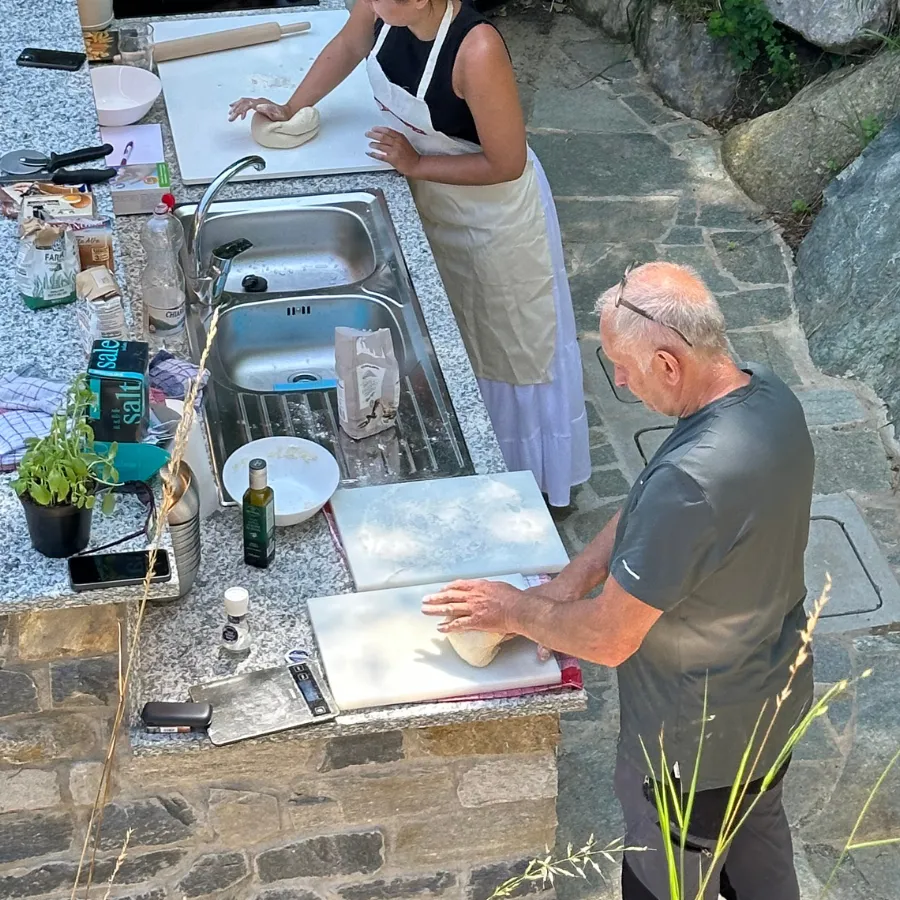Tourists kneading pizza dough at an outdoor kitchen surrounded by nature during a cooking workshop on Lake Como