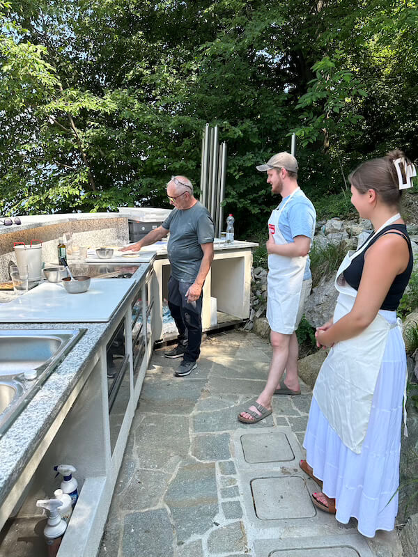 Outdoor cooking class at Baita TreeB in Bellagio, with a chef and guests preparing dough on a stone countertop.