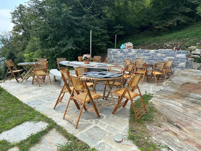 Outdoor dining area with wooden tables and chairs at Baita TreeB in Bellagio, surrounded by greenery.